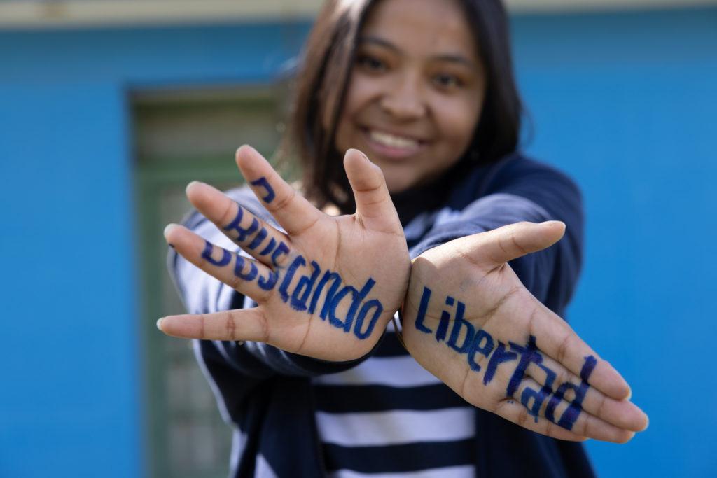 Une jeune fille montre la paume de ses main où il est écrit "Buscando Libertad"